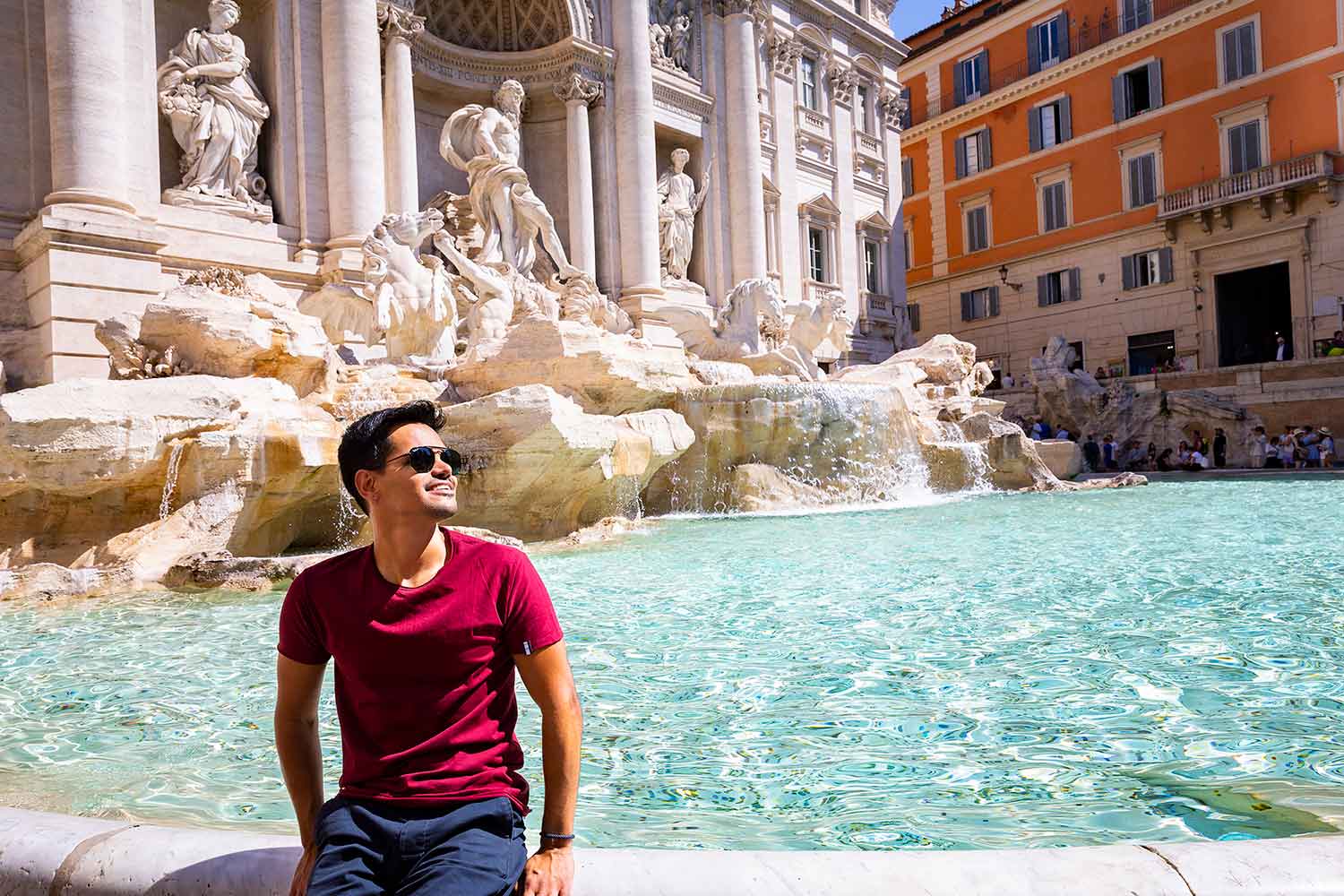 Sitting down portrait picture by the Trevi fountain Rome Italy. With crystal azure water all around