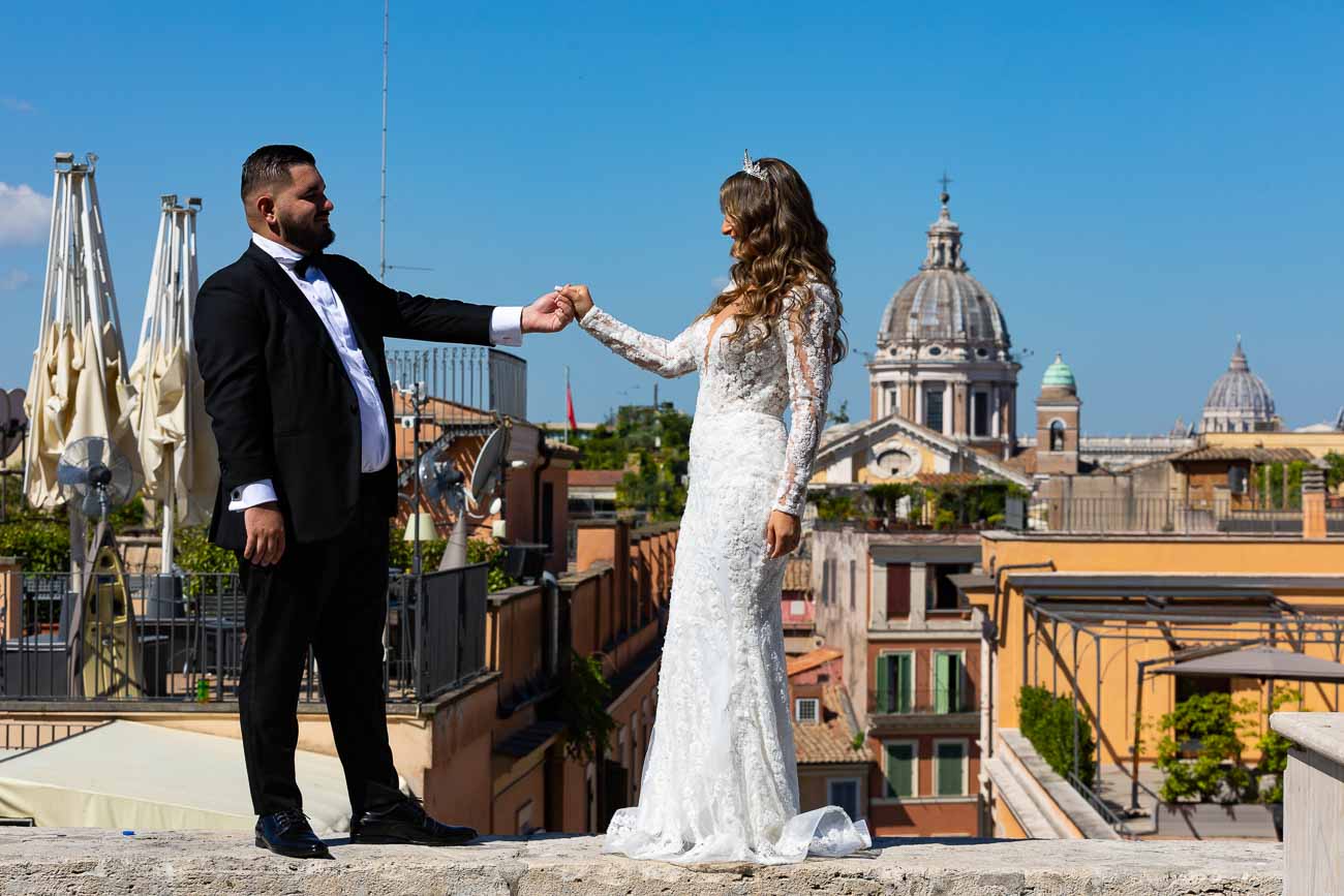 Newlyweds standing together holding hands before the spectacular view of the ancient roman cityscape as photographic backdrop