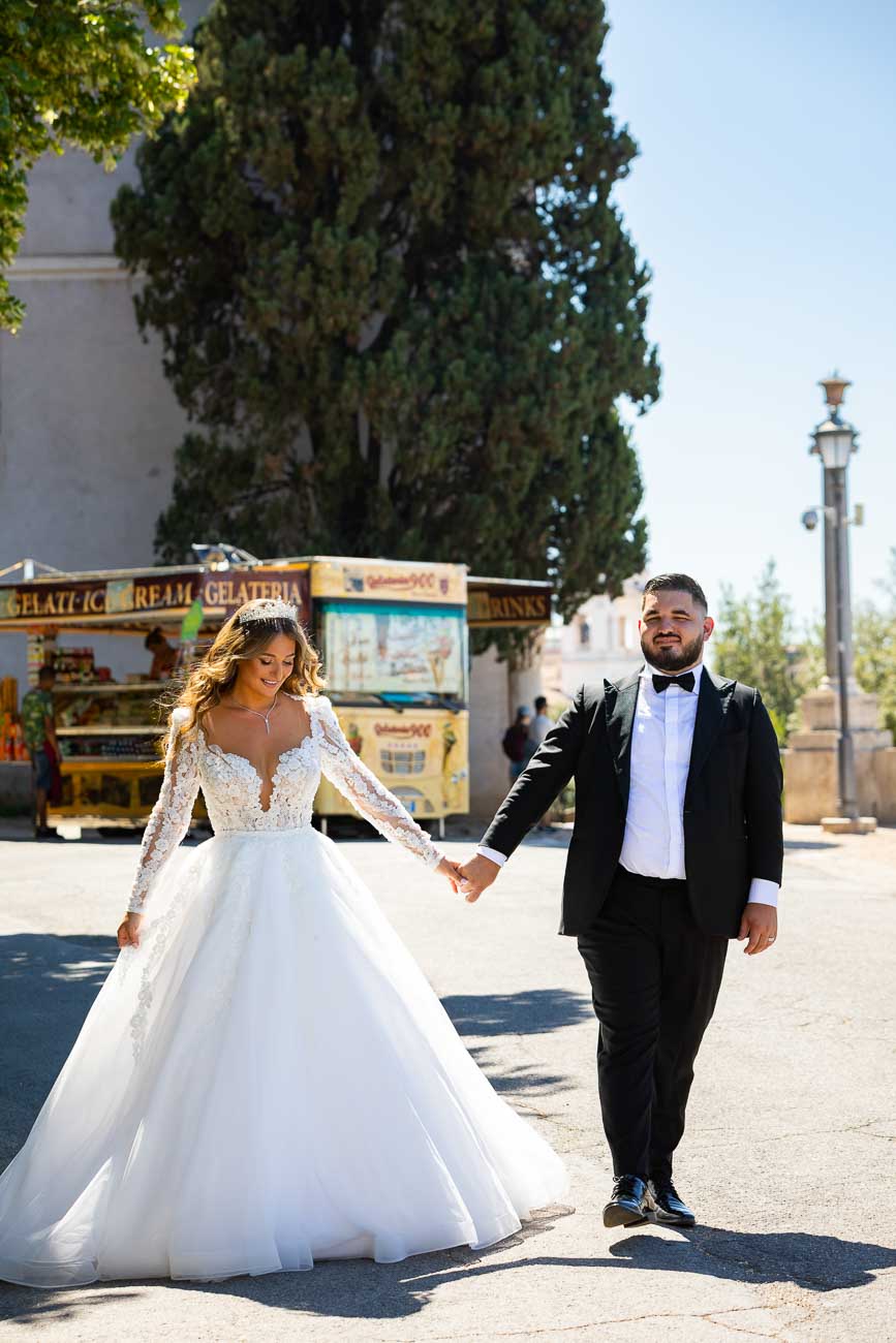 Groom and Bride walking together holdings hands and moving forward at Villa Borghese park