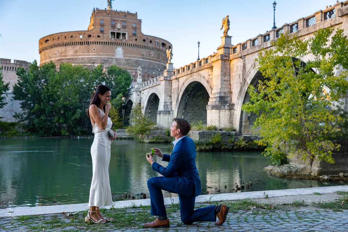Proposing Marriage at Castel Sant'Angelo. Kneeling down for a romantic surprise wedding proposal candidly photographed under the Castel Sant'Angelo bridge in Rome Italy