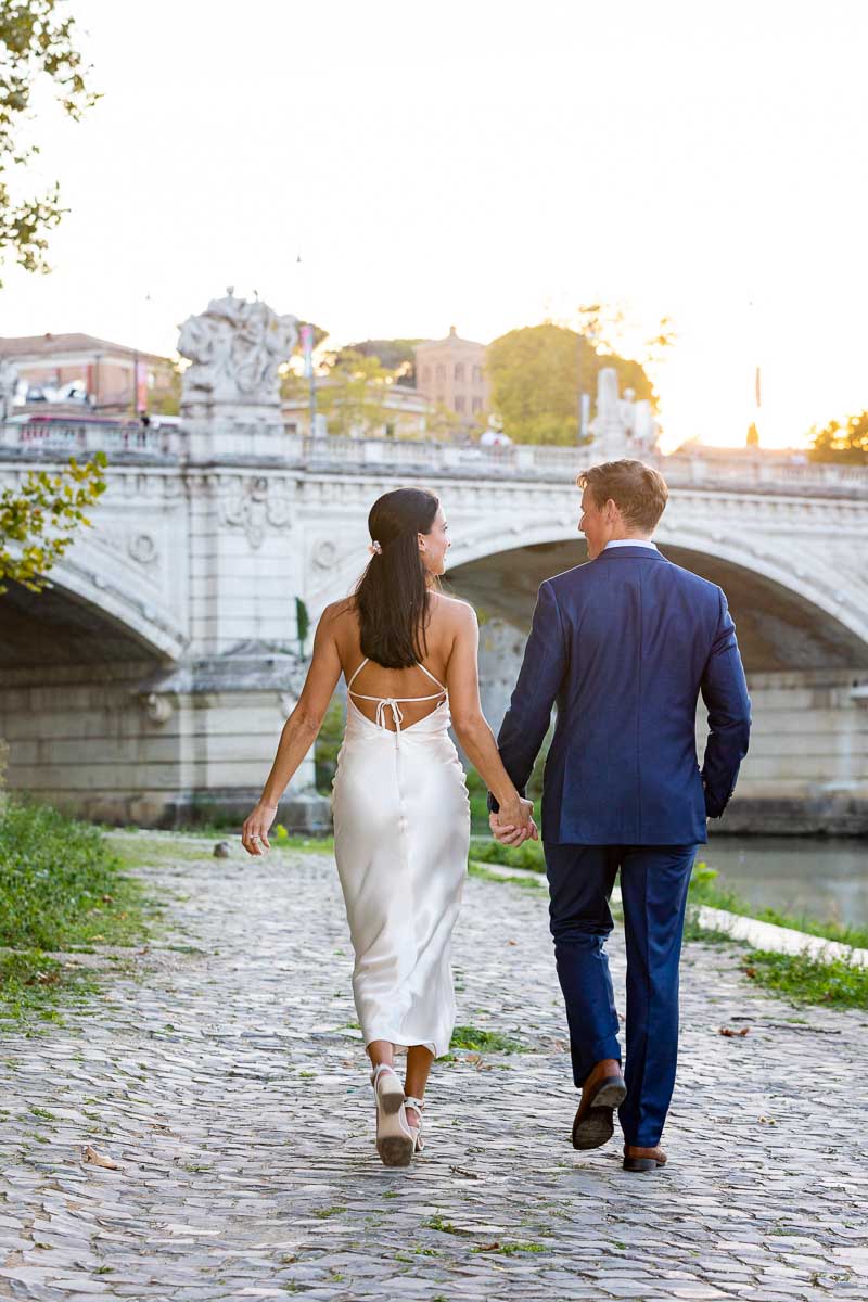 Couple walking hand in hand towards the bridge next to the Tiber river water 