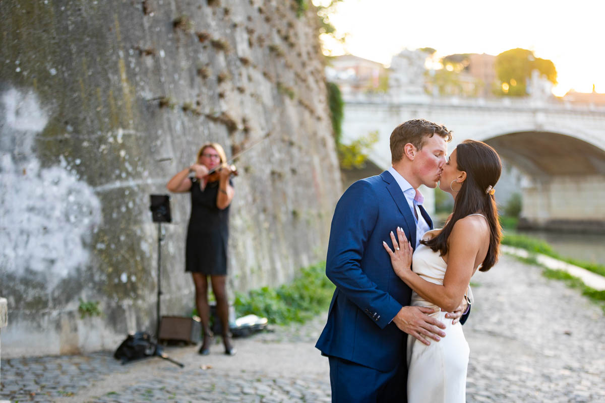 Couple just engaged and kissing with a violinist playing music in the background 