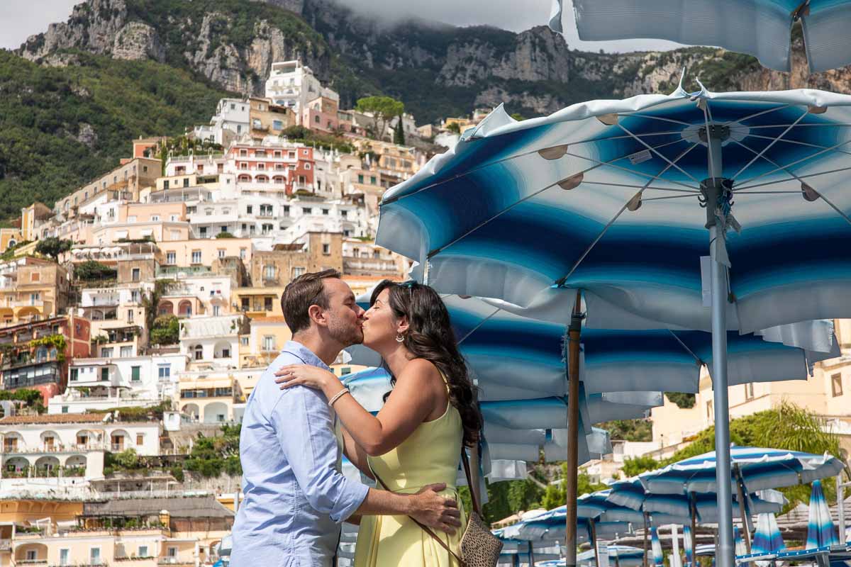 Kissing under the umbrella with the vertical town of Positano as backdrop