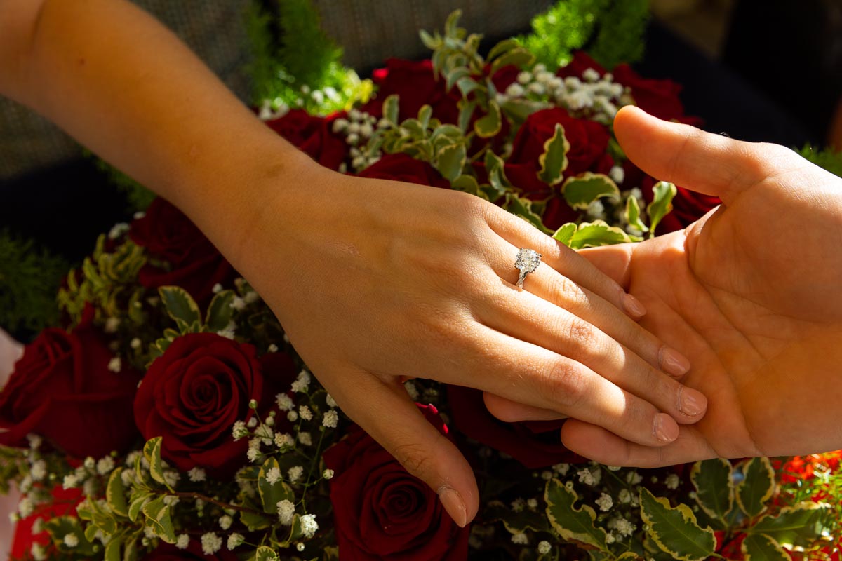 The engagement ring photographed close up in the light over a large bouquet of bright red roses 