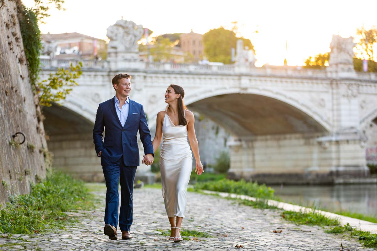 Walking hand in hand next to the Tiber river with a distant bridge in the background