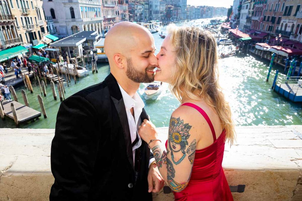 In love in Venice. Kissing on the Rialto bridge with Canal Grande in the far distance in nice sun shining light