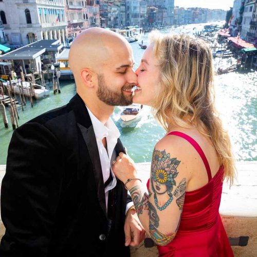 In love in Venice. Kissing on the Rialto bridge with Canal Grande in the far distance in nice sun shining light