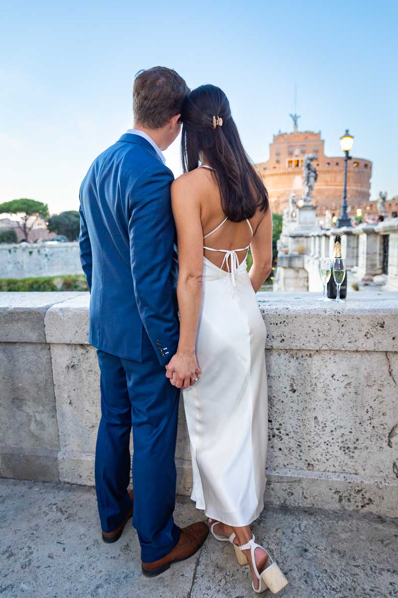 Rear back couple portrait standing together next to one another holding hands and looking at the Castle during sunset