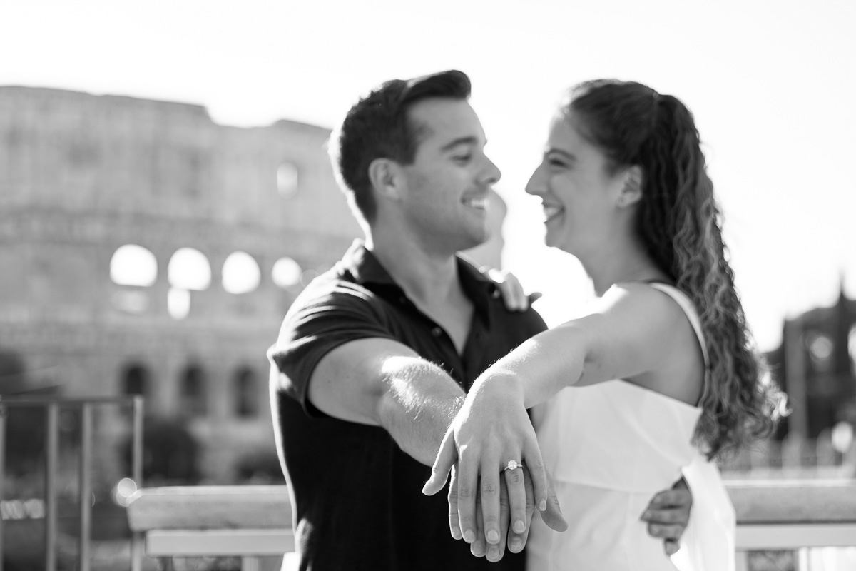 Black and white version of a picture of a couple just engaged showing the beautiful ring before the Colosseum in black and white images