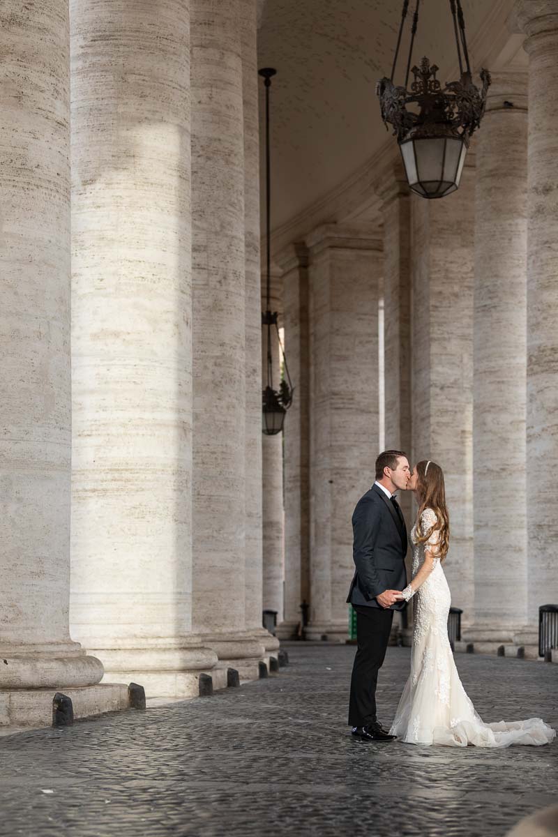 BRide and groom kissing underneath the majestic columns surrounding Saint Peter's square in the Vatican 