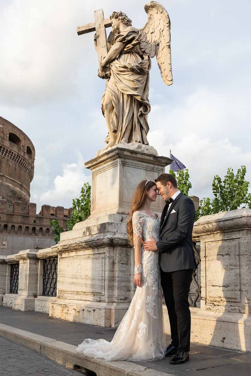 Bride and groom taking pictures on the Castel Sant'Angelo bridge at sunset with lice golden light shining through