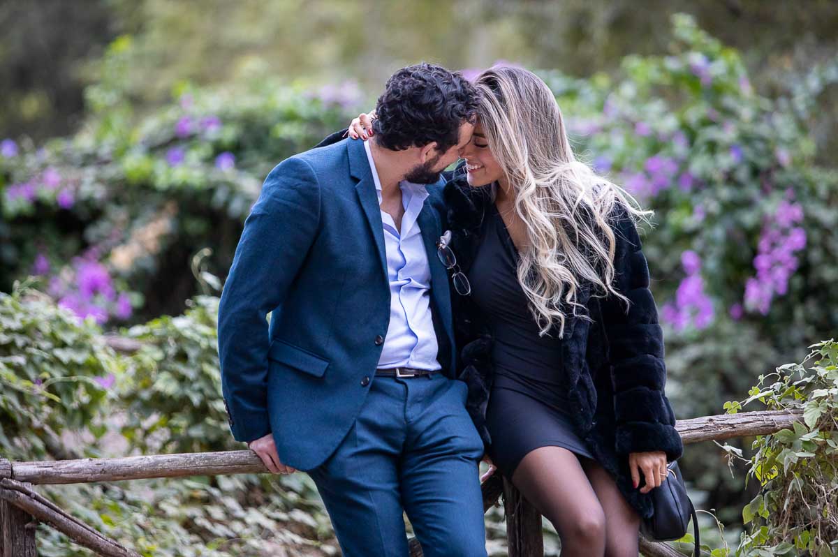 Kissing by bougainvillea flowers while sitting on a wooden fence 