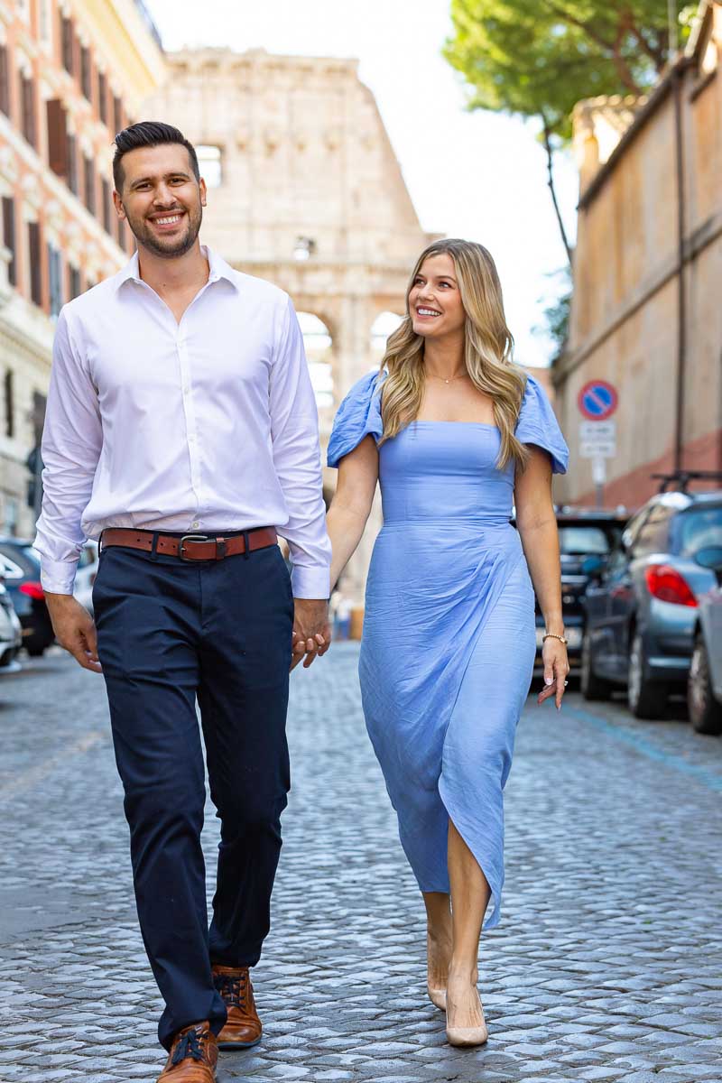 Walking on a roman typical cobblestone alleyway with the Colosseum as backdrop. Rome Engagement Photography