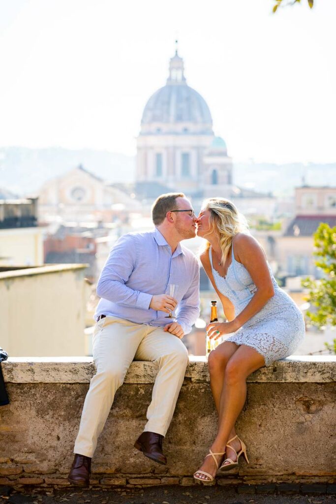 Couple kissing before the roman skyline view while toasting with Italian sparkling wine