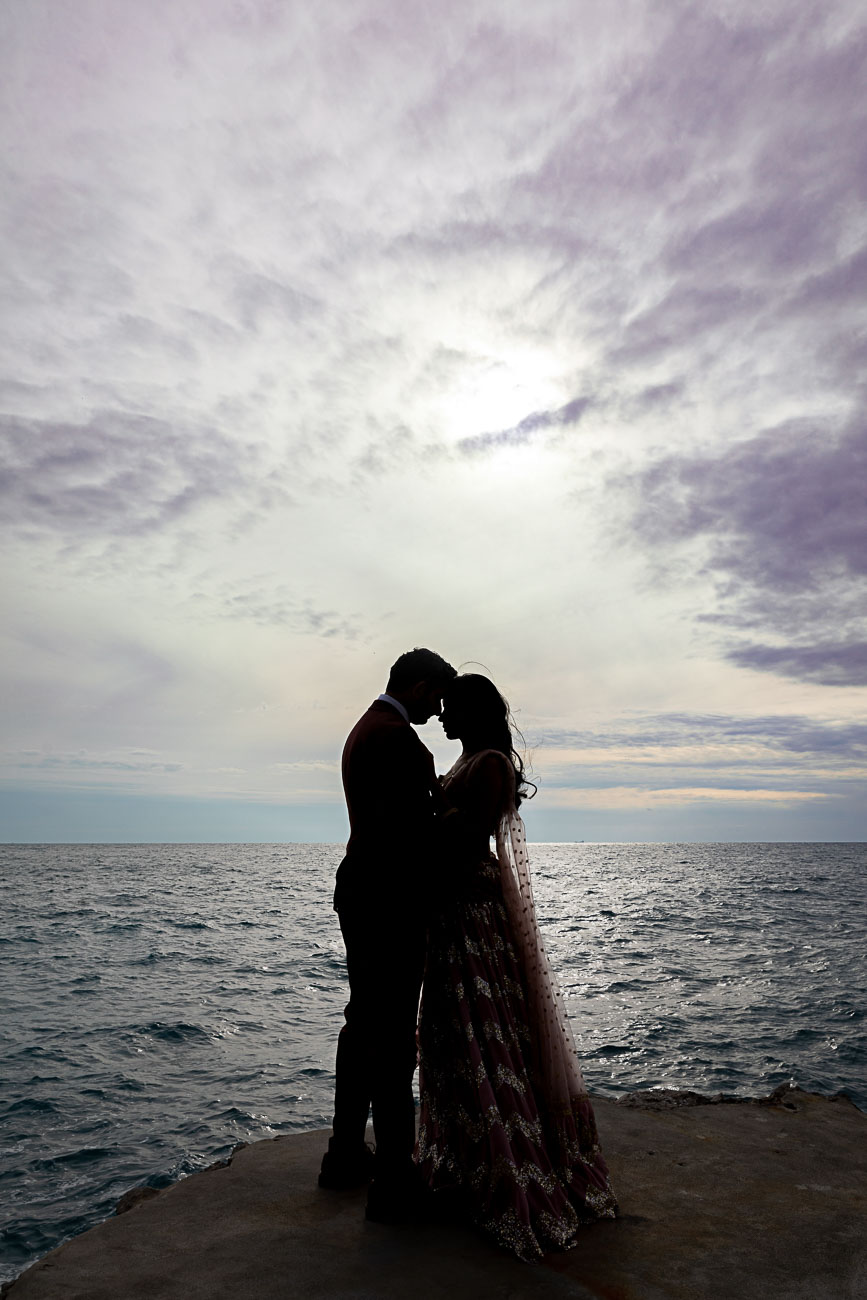 Creative and unique silhouette image of a couple posing in front of the Mediterranean sea resting forehead to forehead 