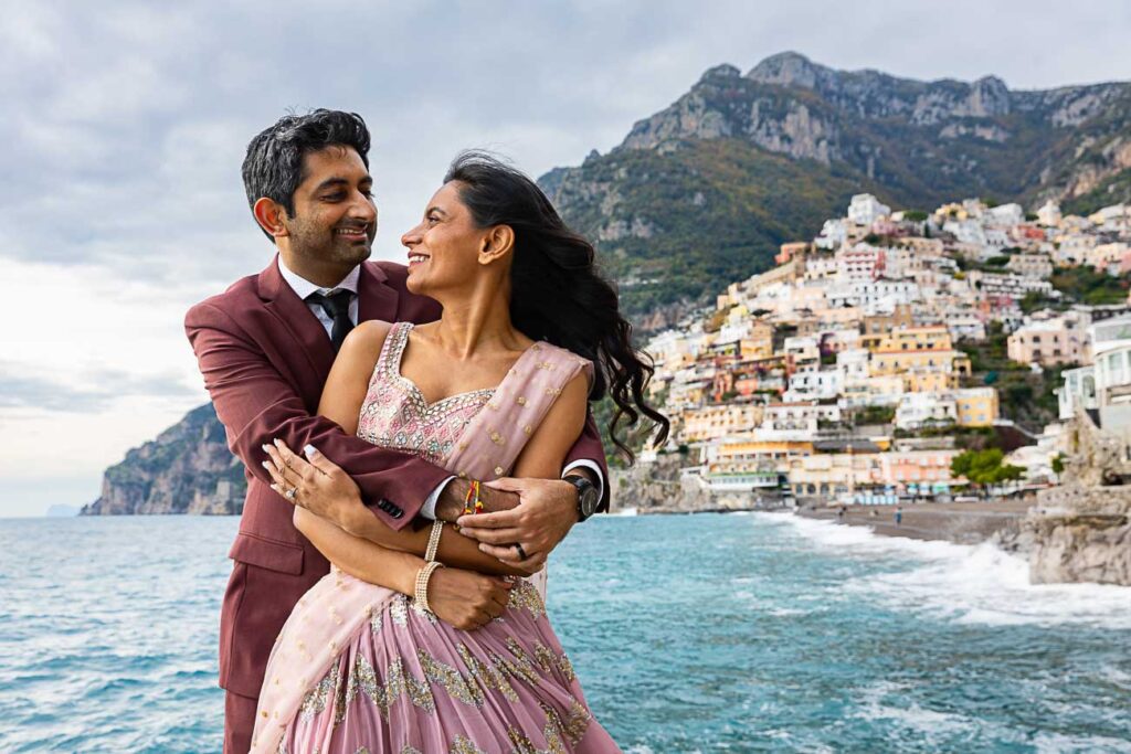 Couple photoshoot in Positano. Bust up portrait picture. Posed on the beach with the town in the far distance