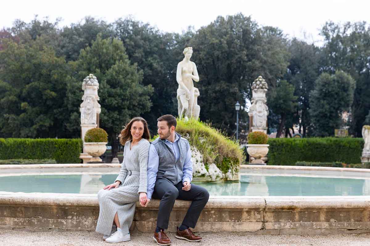 Couple sitting down portrait near the circular water fountain found at the Villa Borghese museum