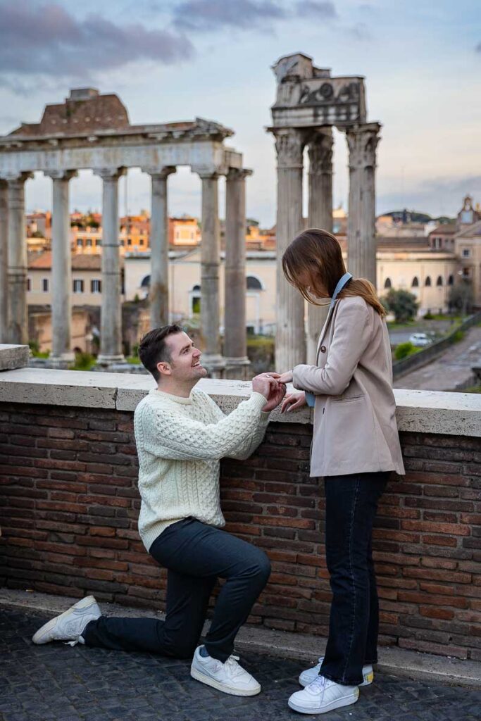 Kneeling down for a surprise wedding proposal candidly photographed at the Roman Forum in Rome Italy