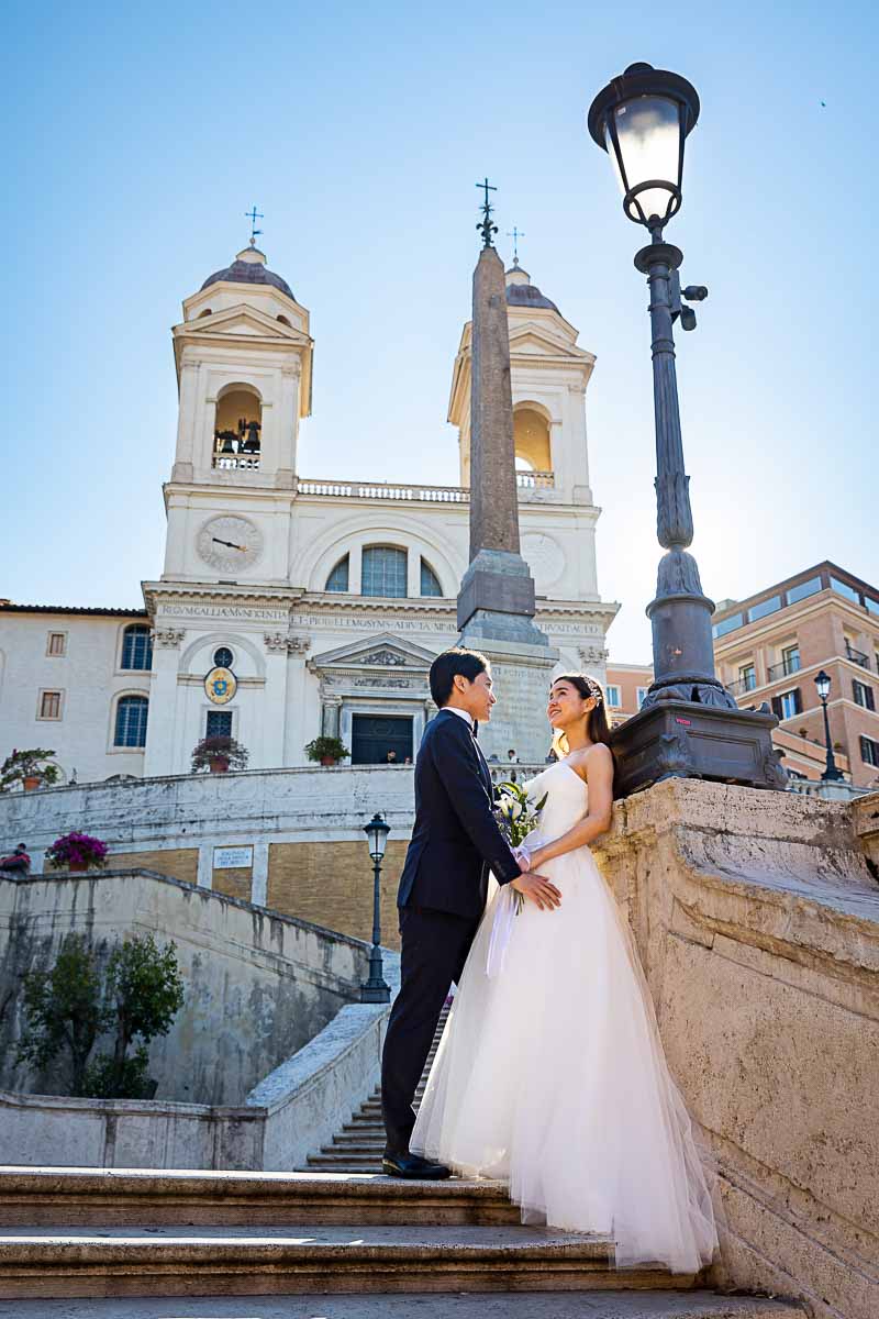 Bride and groom standing on top of the Spanish steps with church Trinita' dei Monti in the background 