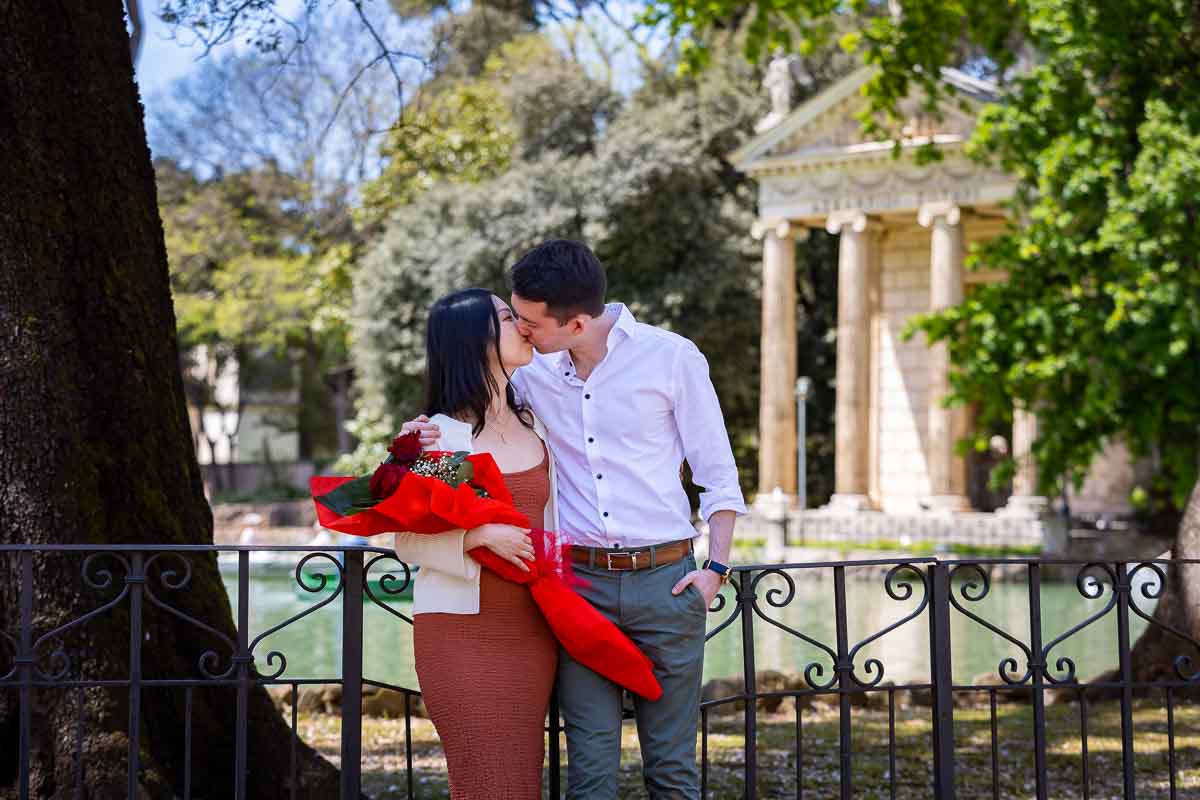 Kissing while holding a bouquet of red roses given to celebrate the engagement photos in Rome
