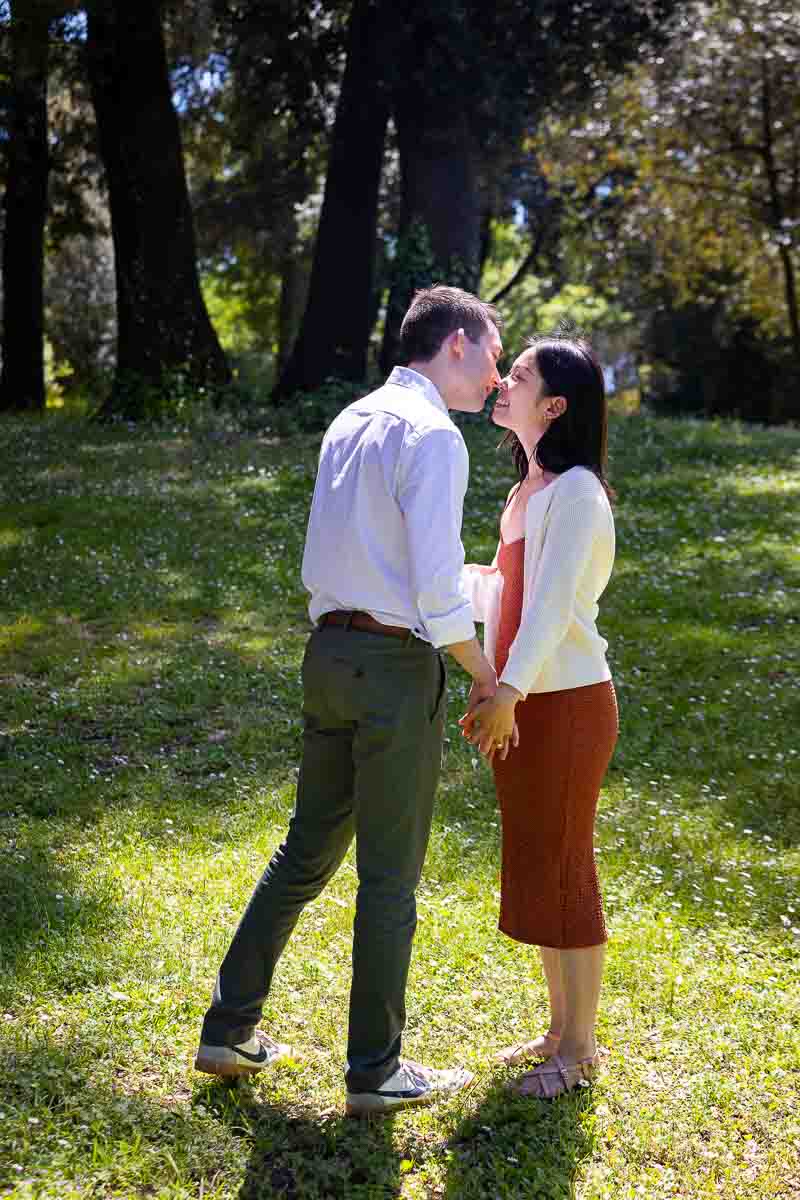Couple just engaged kissing picture in a park with beautiful green grass 