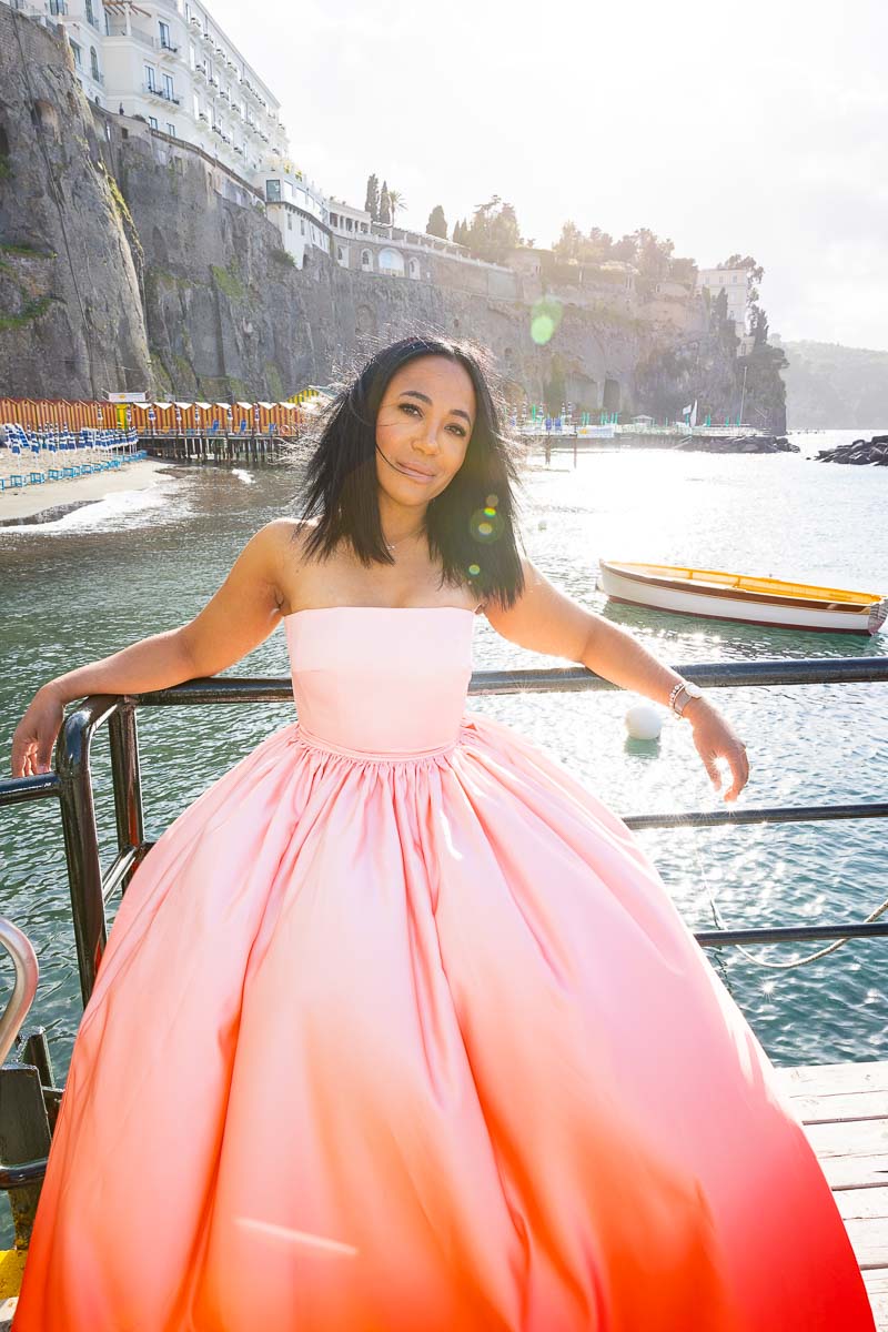 Woman model standing on the edge of sea water taking pictures below the town of Sorrento Italy