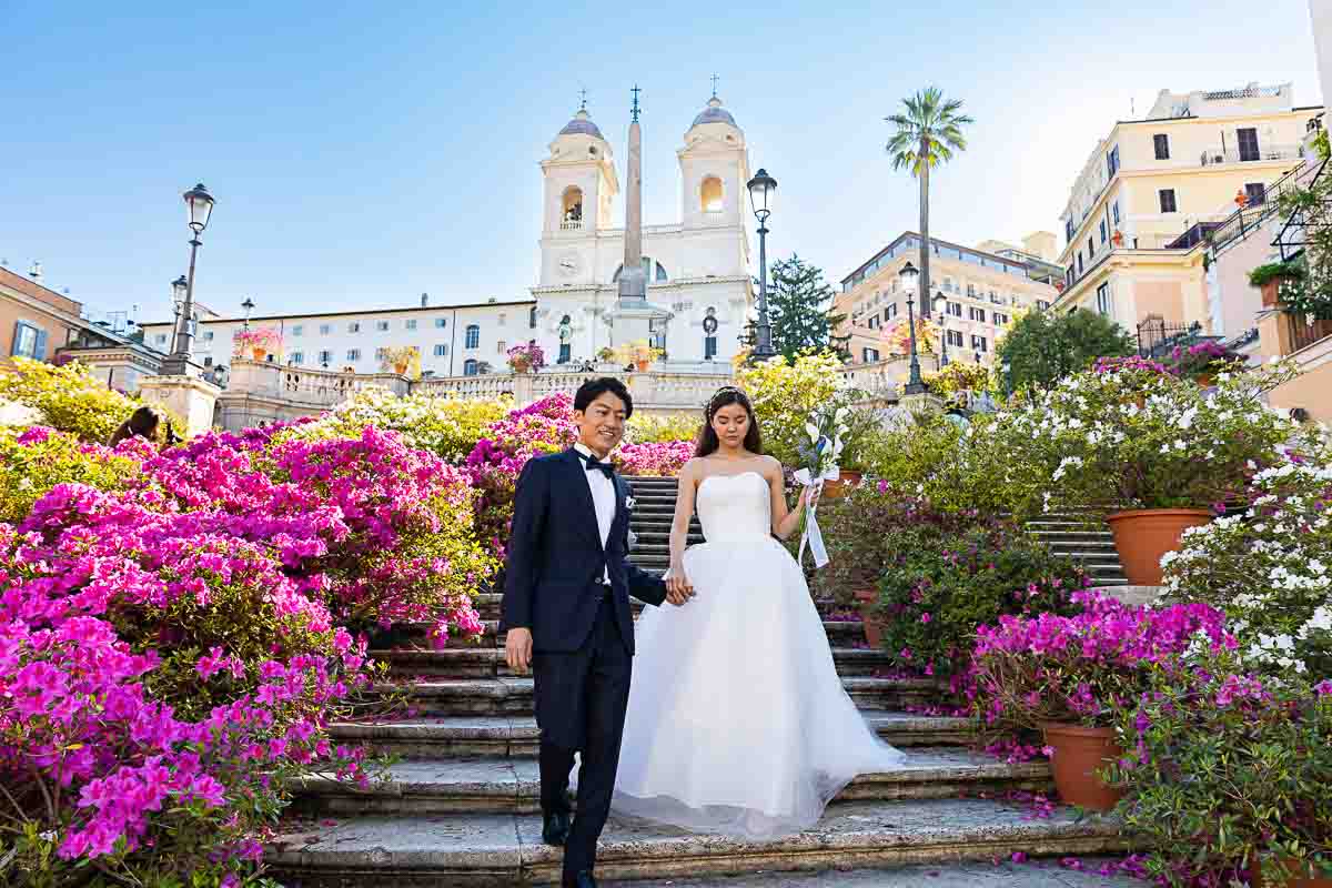 The bride and groom walking down the Spanish steps in spring while the staircase if full of beautiful blossoming flowers 