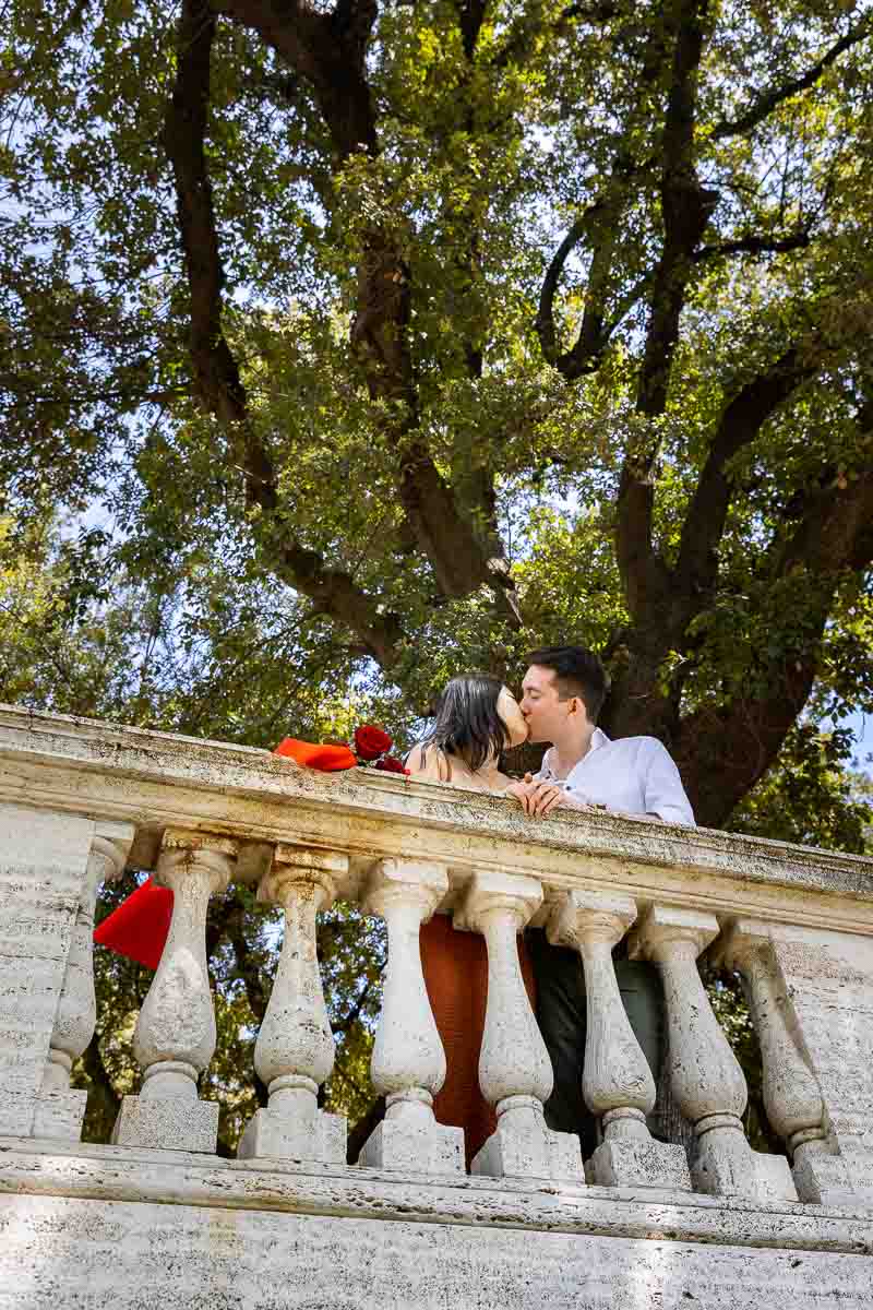 Kissing underneath a green lush tree in the pincio park terrace of Rome 