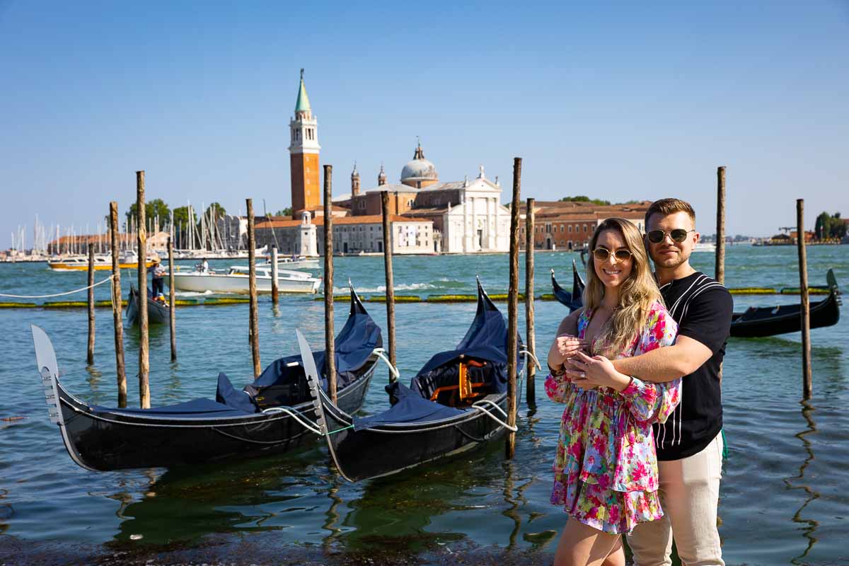 Couple standing next to each other in front of the gondolas docked by the San Marco pier