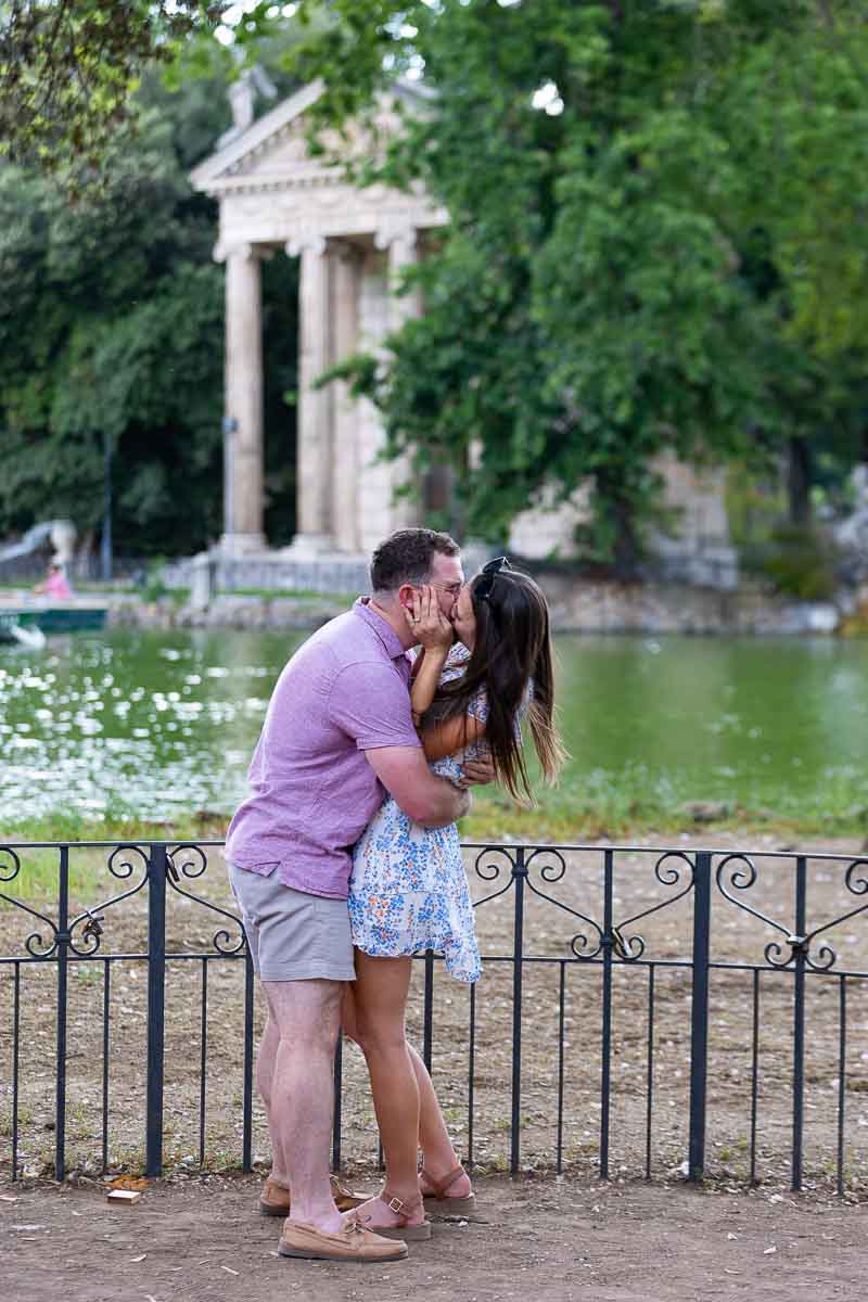 Couple kissing during an engagement photo session following a surprise proposal in Rome at the lake