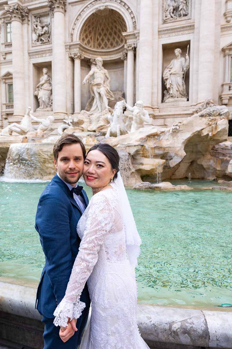 Newlywed couple posing cheek to cheek at Rome's Trevi fountain 