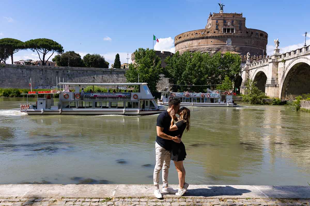 Couple photoshoot in Rome by the Tiber river back with a boats navigating in opposite directions in the background