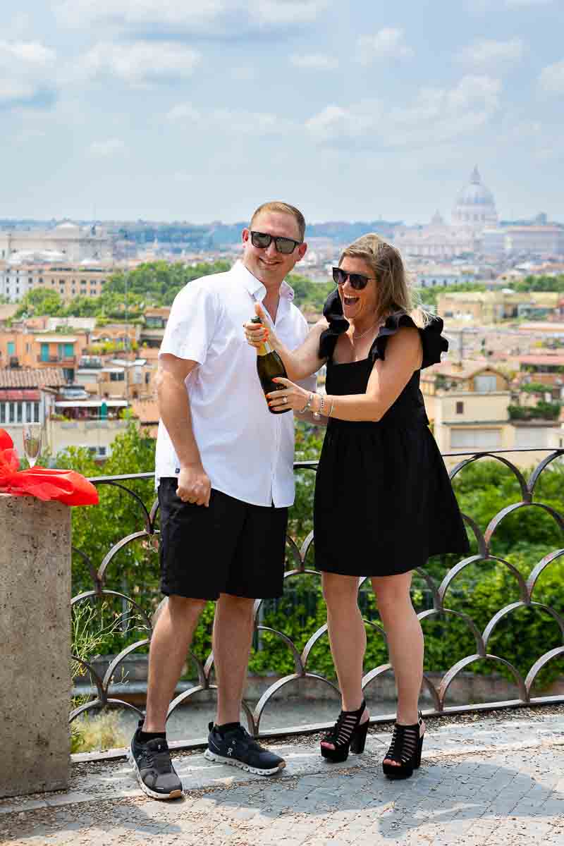 Celebrating engagement with a bottle of Italian sparkling white wine bottle and a bouquet of red roses. Rome Surprise Proposal Photography