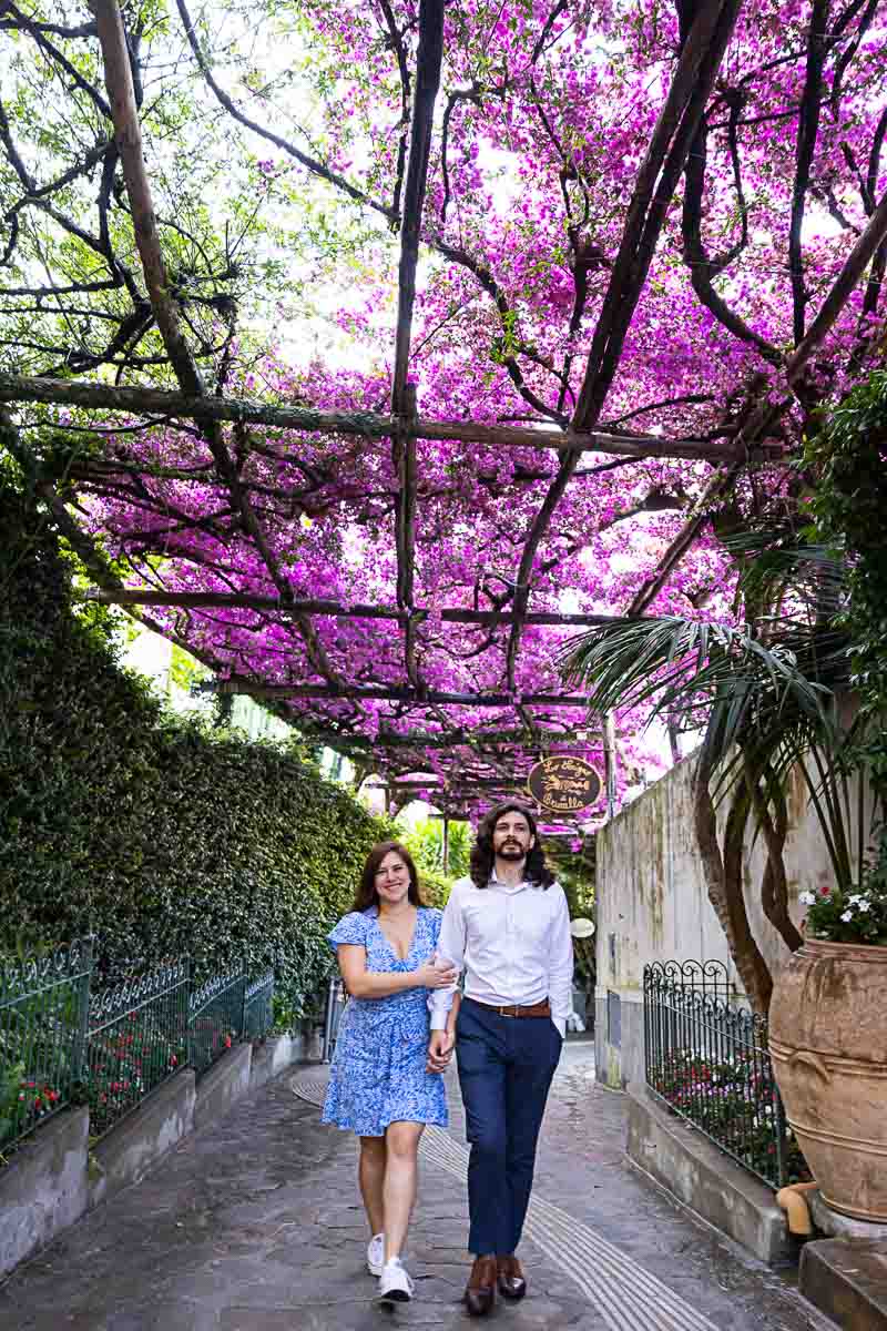 Couple walking under bougainvillea flowers bright fuchsia color over typical alleyway streets 