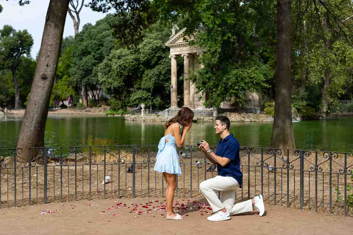 Kneeling down for a surprise wedding proposal candidly photographed in Rome's Villa Borghese lake 