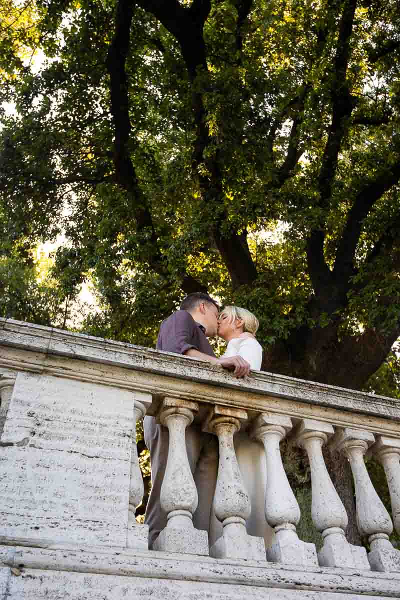 Couple portrait photographed in a park under nice green trees behind a marble balconade 