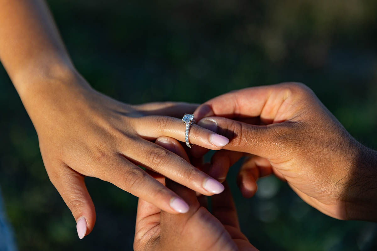 Closeup of the engagement ring as it is being placed on the finger during a surprise wedding proposal