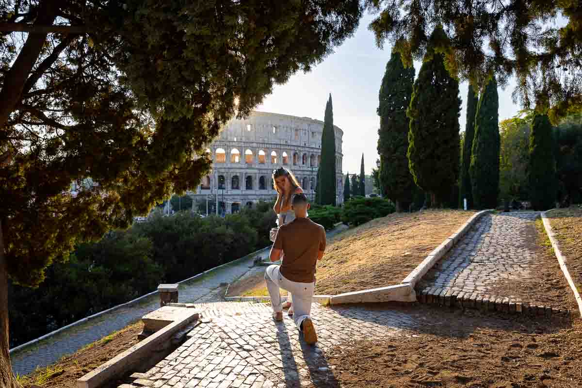 Kneeling down for a surprise wedding proposal at the Roman Colosseum candidly photographed from afar. Exclusive Proposal at the Colosseum