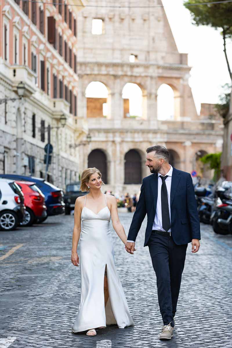 Wedding in Rome. Couple walking hand in hand with the Roman Colosseum in the backdrop