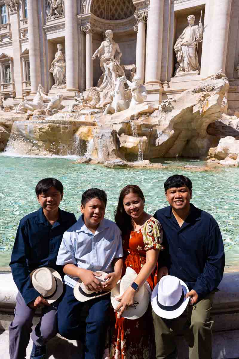 Family sitting down on the edge of the Trevi fountain taking pictures during a Rome photoshoot 