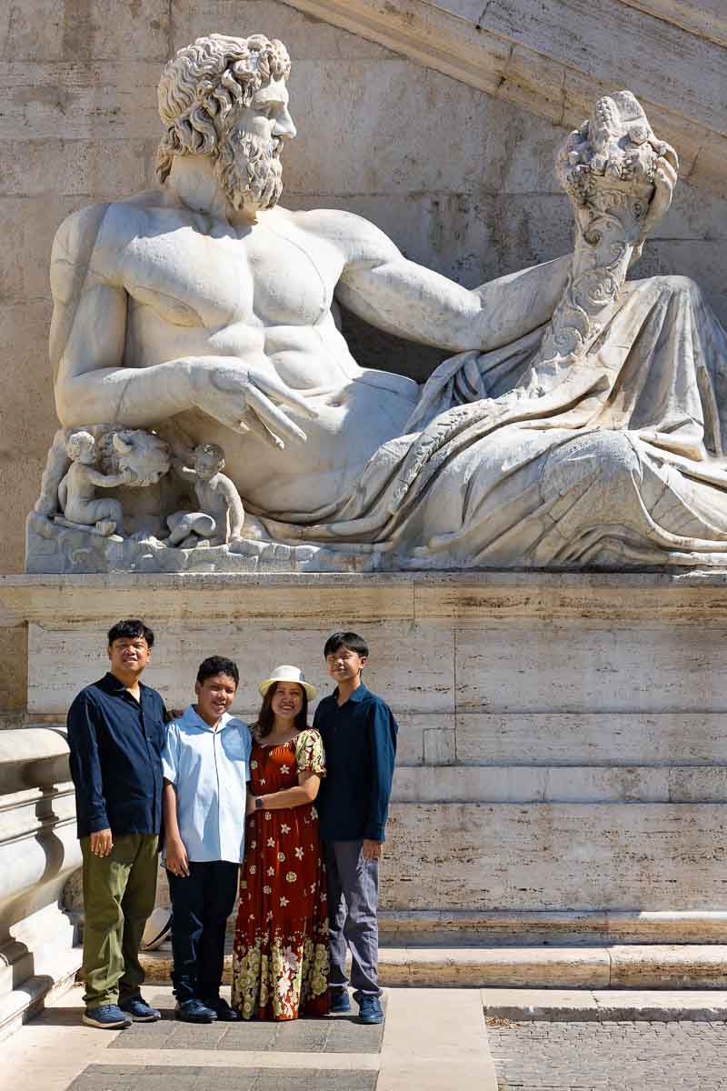 Posed family picture underneath an ancient Roman Marble Statue. Family Vacation Photography in Rome