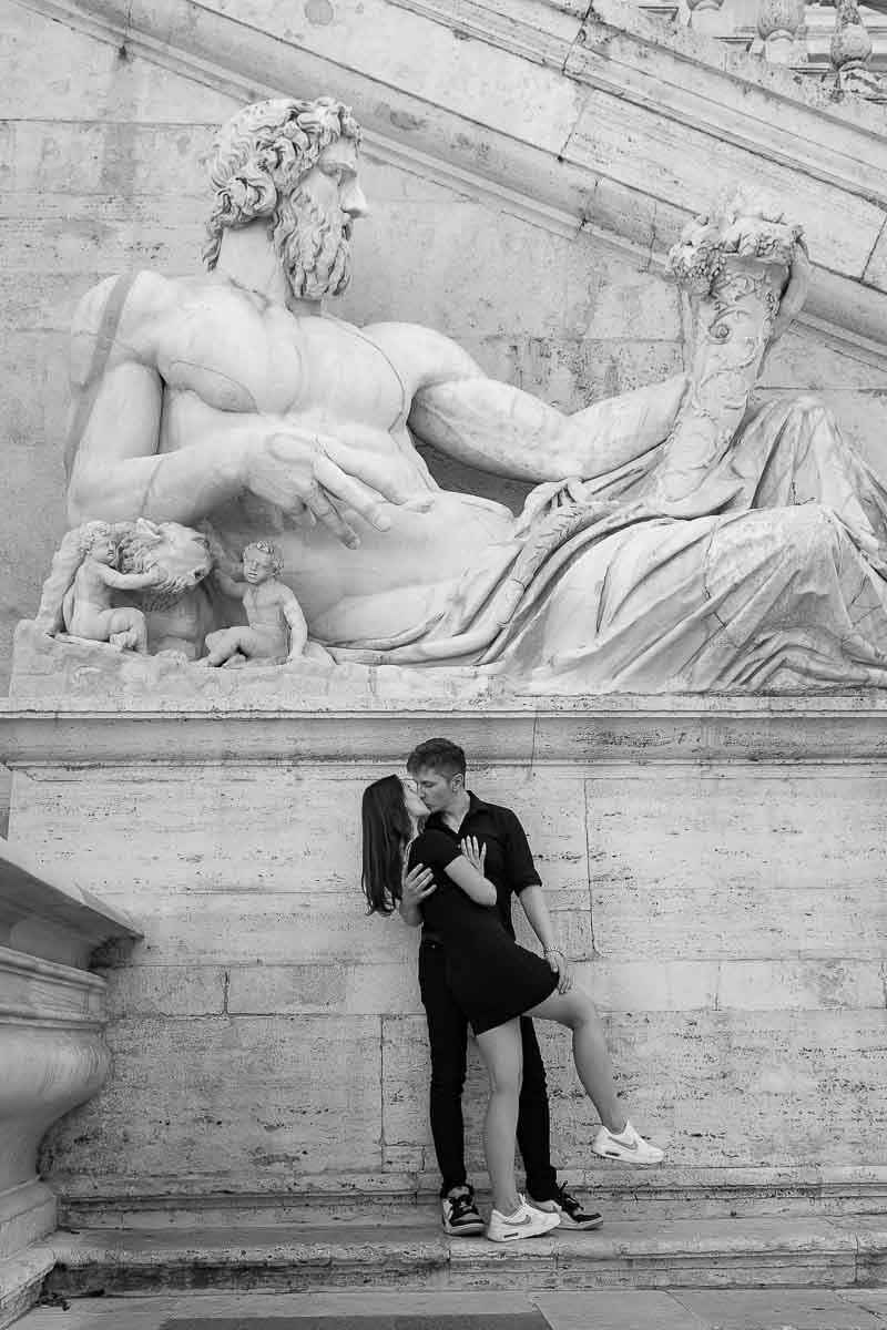 Black and White photography of a couple underneath a very large roman marble statue 