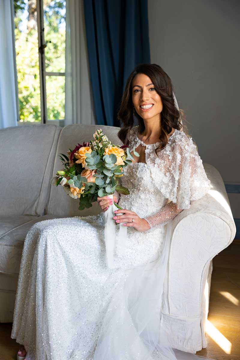 Wedding bride smiling while sitting down and taking bridal pictures by the window