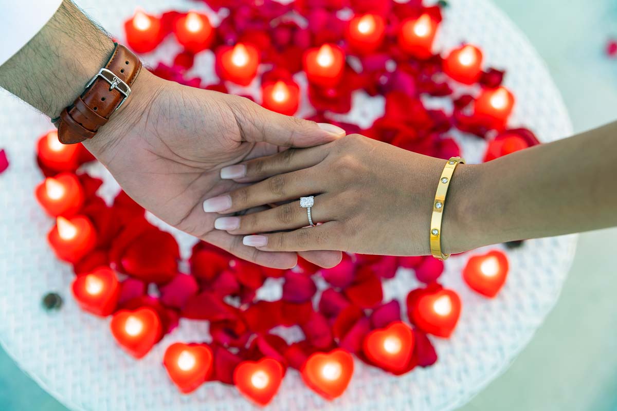 Picture of the engagement ring photographed over red candles and beautiful romantic rose petals 