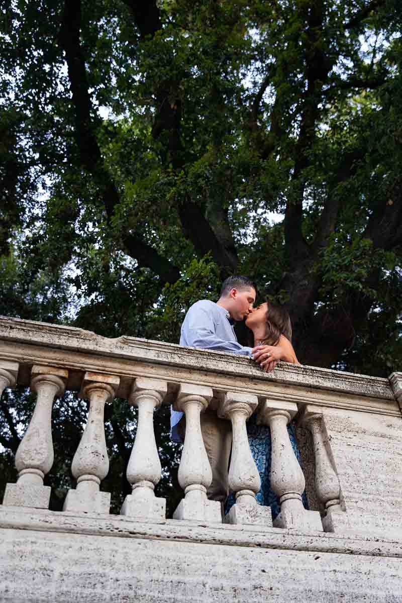 Couple kissing in front of a marble balconade underneath a large park tree