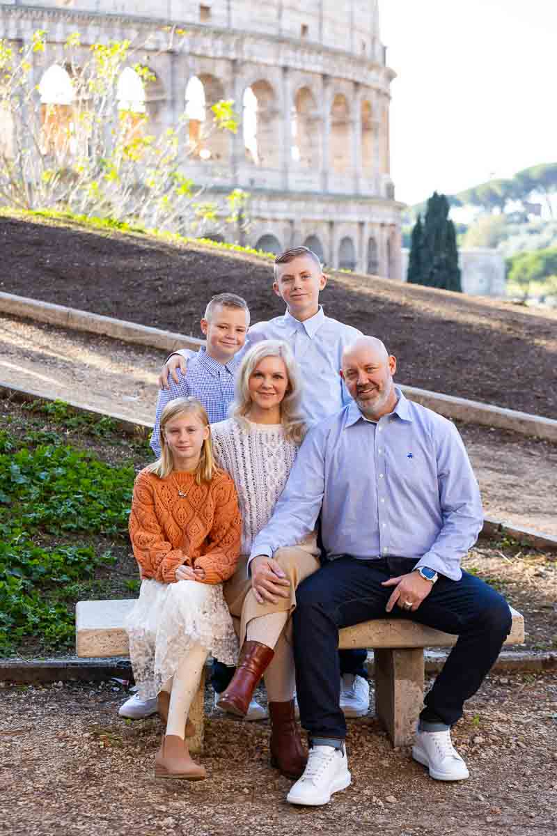 Family portrait sitting down on a marble bench before the view of the Roman Coliseum