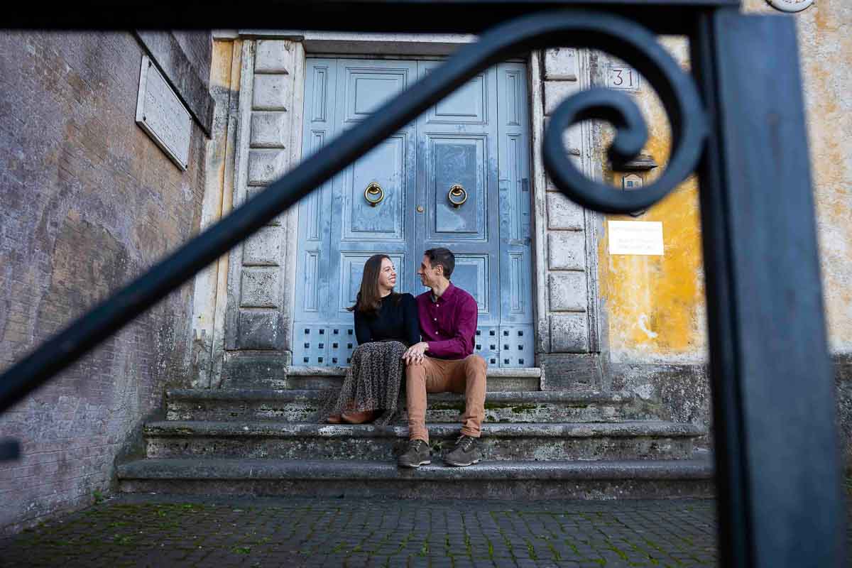 Picture of a sitting down couple by a colorful doorway and building through a metal railing 