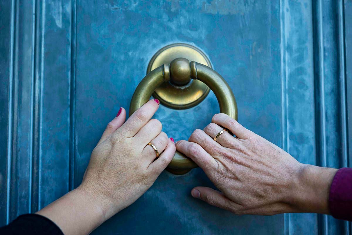 Couple holding on to a blue door ring with their engagement rings on 