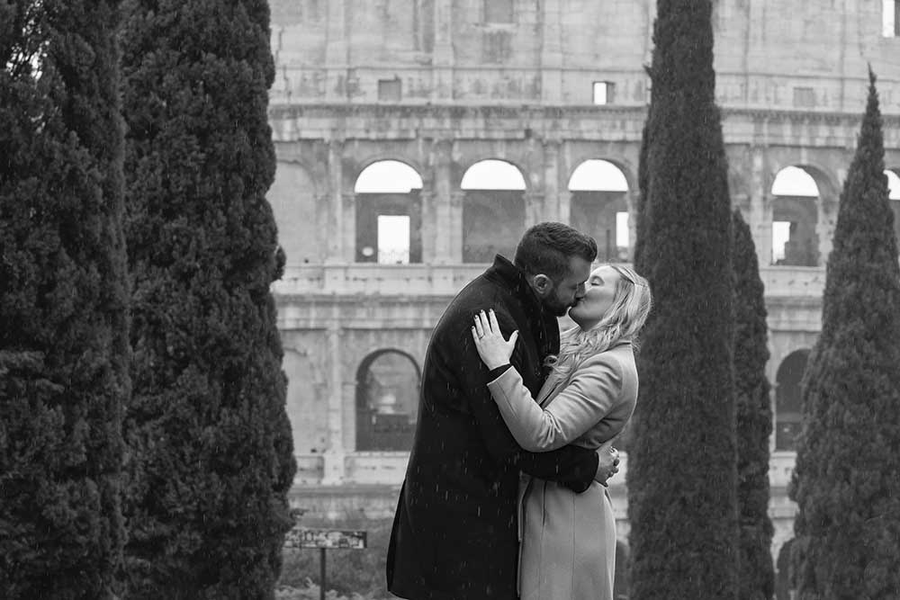 Couple engagement photo shoot in Rome kissing under drizzling rain by the Roman Colosseum