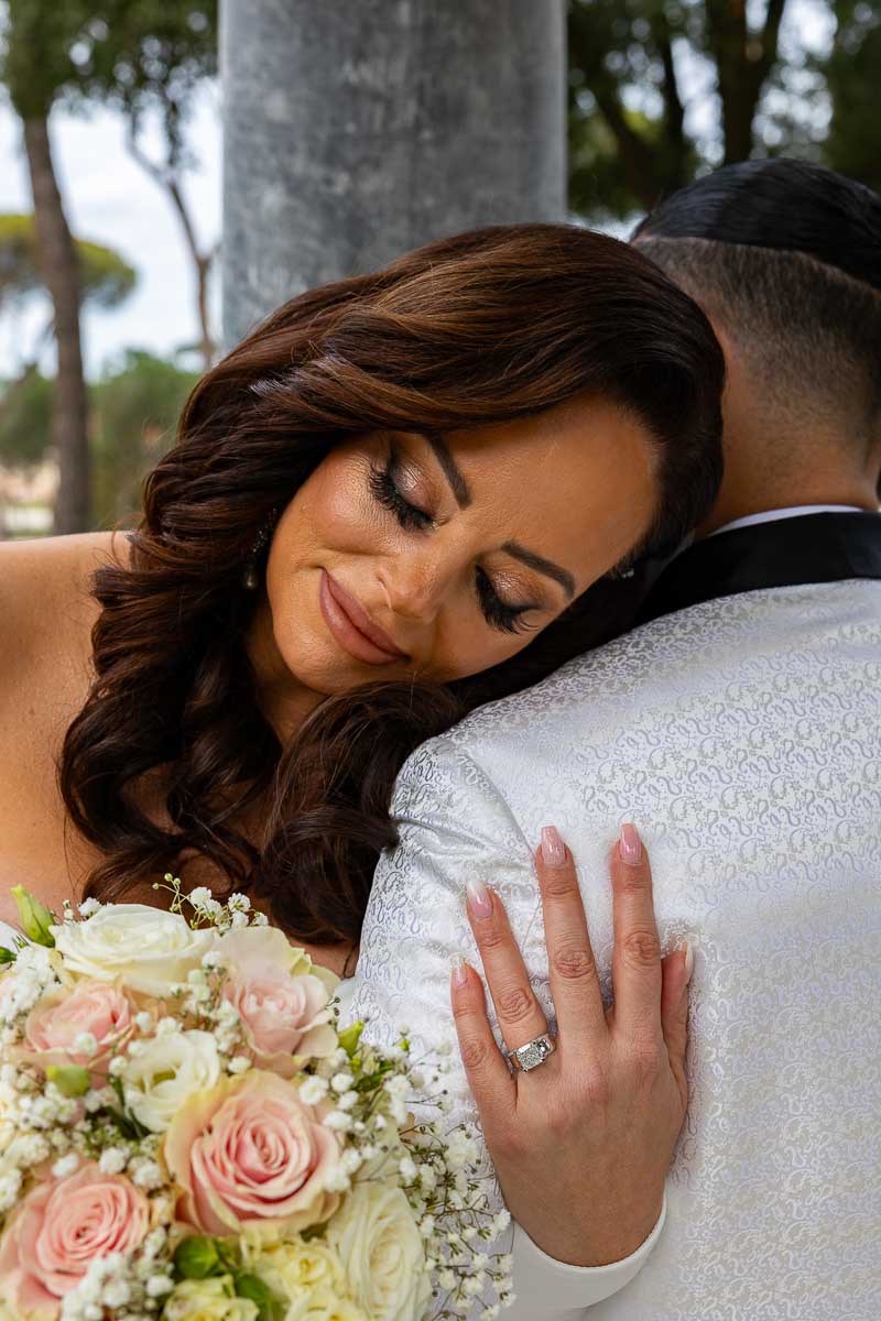 Bridal facial photo with the wedding bouquet and the anniversary ring resting on the groom shoulder